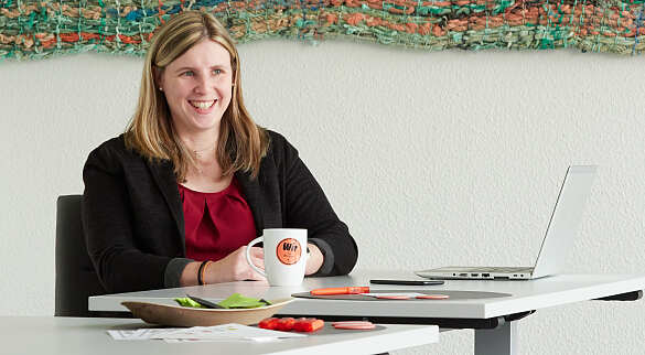 Carina Jahn sitzt am Tisch und lacht. Vor ihr steht eine Tasse mit der Beschriftung Wir für Bremen.