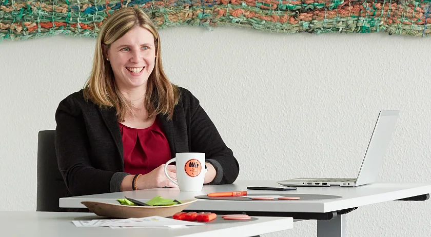 Carina Jahn sitzt am Tisch und lacht. Vor ihr steht eine Tasse mit der Beschriftung Wir für Bremen.