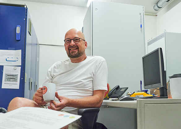 Stefan Last sitzt an einem Arbeitsplatz. In der Hand hält er eine Tasse mit Wir für Bremen- Logo.