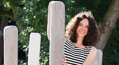 Eine Frau mit dunklem, lockigen Haar steht draußen auf einem Klettergerät aus Holz