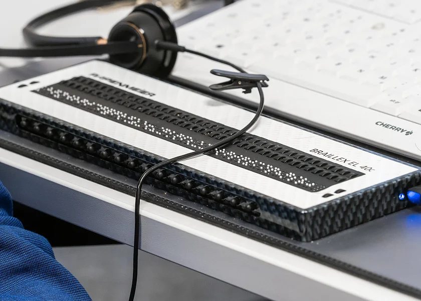 Das Hilfsmittel Braille-Zeile liegt auf dem Schreibtisch vor einer handelsüblichen Computer-Tastatur