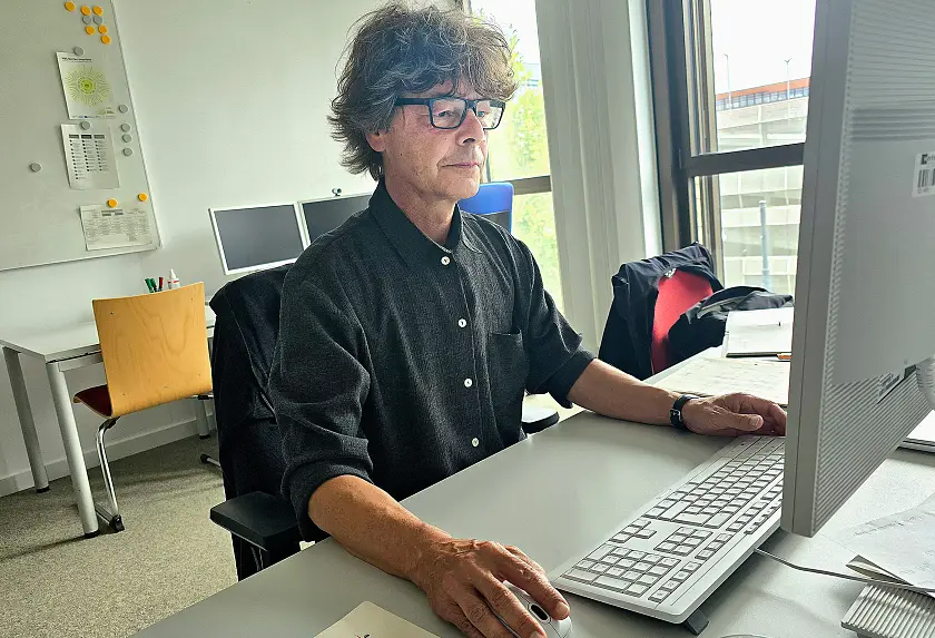 Stefan Wittig sitzt im dunklen Hemd und mit Brille an seinem Arbeitsplatz vor dem Computer