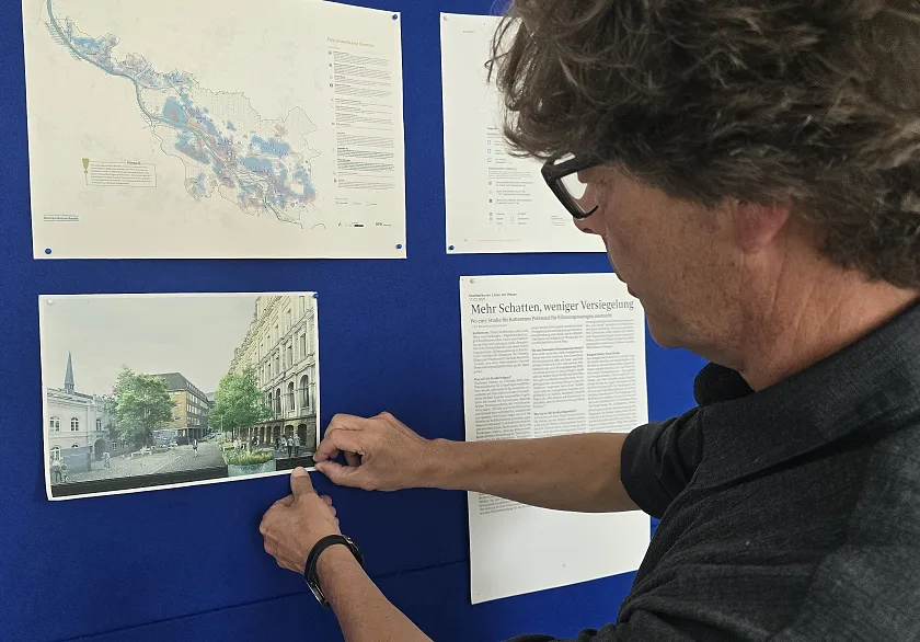 Stefan Wittig steht vor einer blauen Pinnwand und hängt eine Visualisierung des Klimaanpassungsprojekts in der Bremer Dechanatsstraße auf