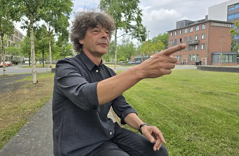 Stefan Wittig sitzt vor seiner Arbeitsstätte in der Überseestadt auf einer Sitzgelegenheit und deutet mit dem Finger nach vorn.