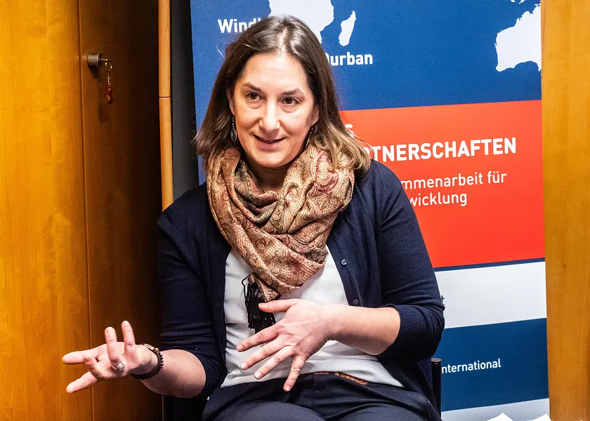 Randy Haubner gestikuliert, sie trägt schulterlange braune Haare, eine blaue Strickjacke und einen Schal um den Hals