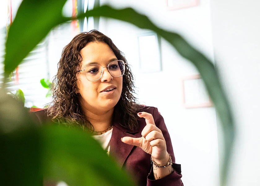 Das Bild zeigt Sarah Roba im Gespräch. Im Vordergrund befindet sich eine Pflanze.