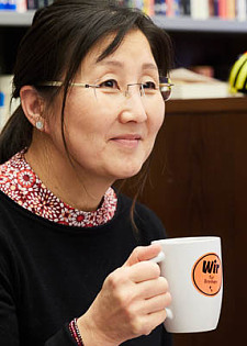 Tina Echterdiek mit schwarzem Pullover in der Seitenansicht. Sie hält eine Tasse mit der Aufschrift Wir für Bremen in der Hand.