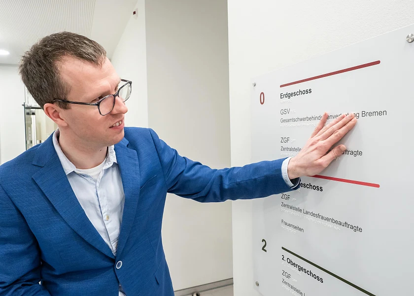 Christian Dabs steht vor einem Leitsystem in einem Treppenhaus und liest mit seinen Fingerspitzen die Braille-Schrift