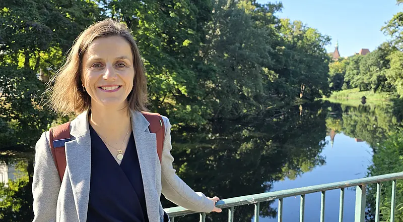 Lachende Frau auf einer Brücke in den Wallanlagen mit hellgrauem Blazer