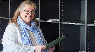 Yvonne Burke hält eine Umlaufmappe in der Hand und steht vor den Postfächern des Standortes.