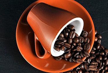 Orange Kaffeetasse auf einem Unterteller, aus der Kaffeebohnen geschüttet werden