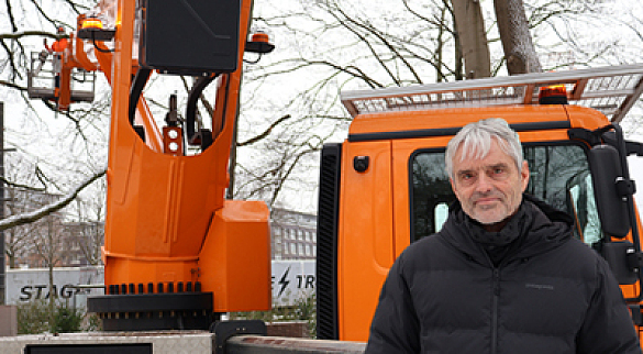 Der grauhaarige Landschaftsarchitekt Günter Brandewiede steht vor einem orangefarbenen Baustellenfahrzeug