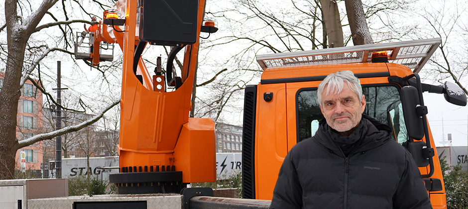 Der grauhaarige Landschaftsarchitekt Günter Brandewiede steht vor einem orangefarbenen Baustellenfahrzeug