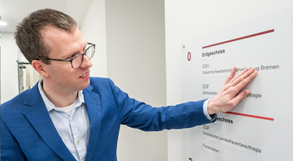 Christian Dabs steht vor einem Wegleitsystem in einem Flur und ertastet mit seiner Hand die Braille-Zeile