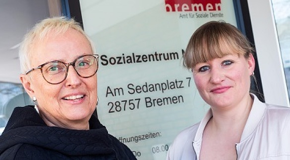 Lebensältere Frau mit blonden kurzen Haaren und Brille, Verena Stolczewski, neben junger Frau mit mittelblonden Haaren und Pony, Madlen Loske, vor dem Eingang des Amts für Soziale Dienste in Bremen-Vegesack