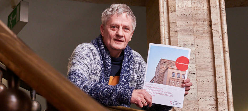 Foto von Werner Fechner von der Betrieblichen Suchtkrankenhilfe im Treppenhaus. In der Hand hält er die Dienstvereinbarung zur Suchtprävention.