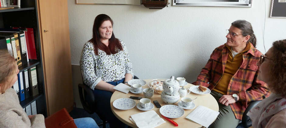 Rebecca Miller und Michael Schnelle sitzen an einem runden Tisch, der mit einem Teeservice gedeckt ist.